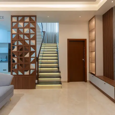 Duplex living room where a teak triangular-lattice jaali screens the white kitchen and a stone staircase with LED-lit risers climbs beside a TV wall of