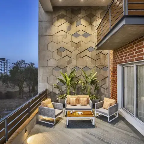 Dusk shot of a deep apartment terrace where a honeycomb of hexagonal concrete tiles rises behind a white-framed outdoor sofa