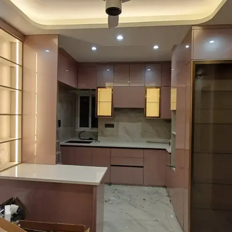 Dusty-rose high-gloss L-shaped kitchen at handover stage, with gold-framed backlit display niches in the wall units