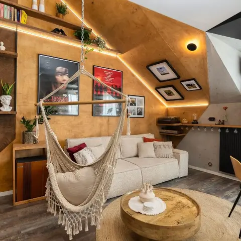 Eclectic attic living room with a hanging macrame swing chair in front of an angular wood-clad accent wall, framed movie posters, an open bookshelf