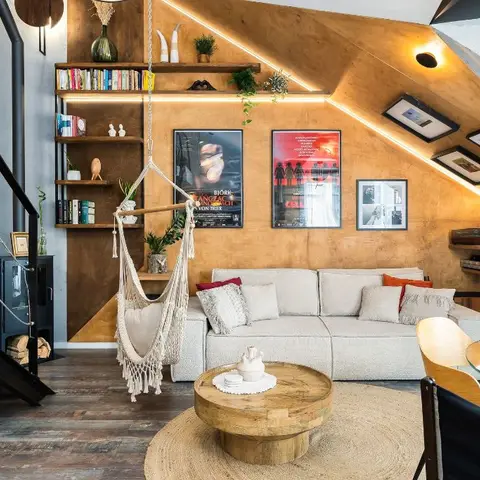 Eclectic attic loft living room under a warm plywood-clad sloped ceiling with LED edge lighting, a macrame hammock chair beside open wood shelving