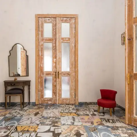 Eclectic entrance hall with a graphic-print patchwork tile floor, distressed timber-and-glass double doors, a vintage arched mirror over a wood console