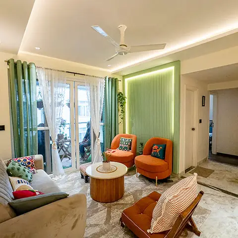 Eclectic living room with a cove-lit sage-green fluted panel accent wall, terracotta armchairs with printed cushions and layered green and sheer curtains onto