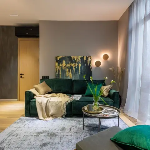 Emerald-green velvet sofa with a beige throw and layered grey rug, round brass-framed coffee table