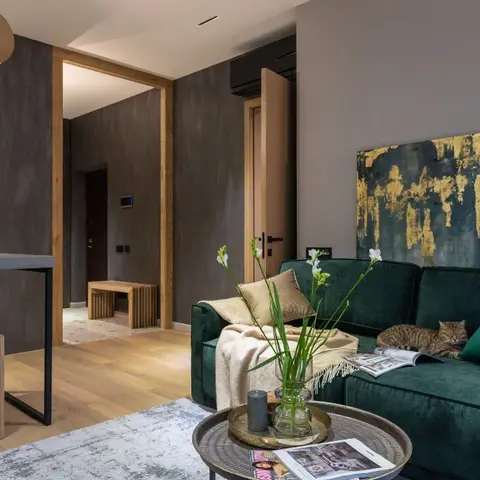 Emerald velvet sectional sofa beneath a large gold-leaf abstract painting, with a concrete kitchen counter and wood floors beyond.