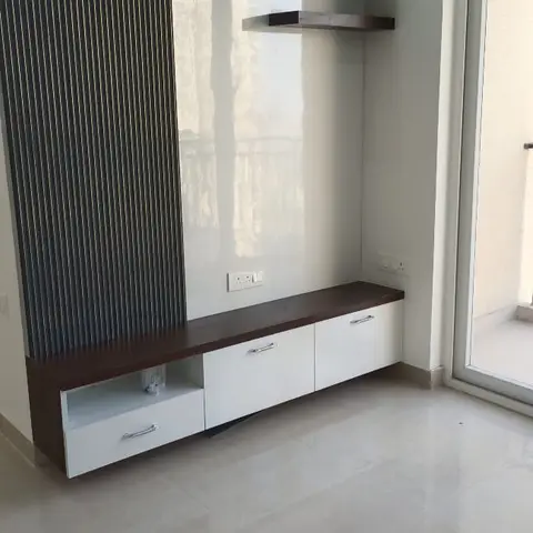 Empty apartment corner with a low wenge-and-white TV console below a mirrored glass panel and fluted wood cladding strip, floating shelves