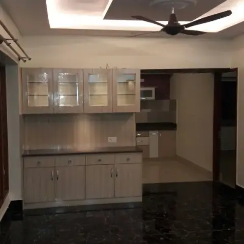 Empty dining space at handover with a light-oak crockery unit against a rectangular cove-lit POP ceiling and black marble flooring, kitchen doorway beyond