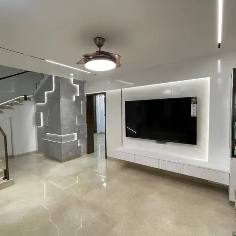 Empty duplex living hall with a backlit white stone TV panel over a fluted floating console, a grey stone-clad staircase column routed with LED slots