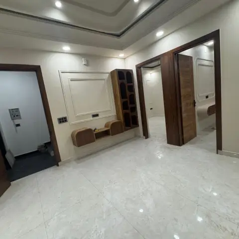 Empty entrance foyer with a dark wood-framed main door, a white panel-moulding wall, a floating wood console with cutout display shelving