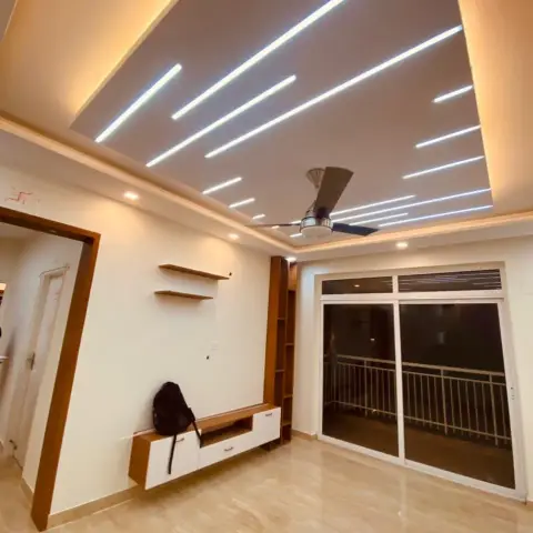 Empty living room at handover under a taupe false ceiling fanned with slim linear LED profiles