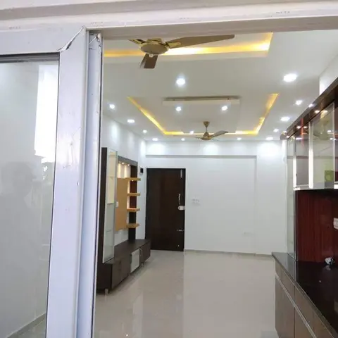 Empty living room seen through the entrance door, with a two-tier cove-lit false ceiling and a glossy maroon TV/display unit along the side wall.
