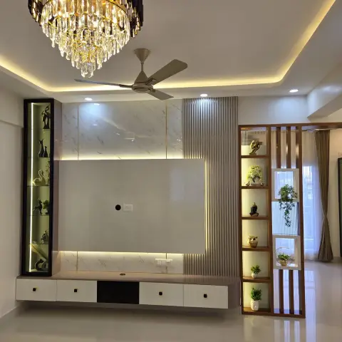 Empty living room where a black-and-gold crystal chandelier hangs beside the ceiling fan over a TV wall of white marble slab with gold inlay lines