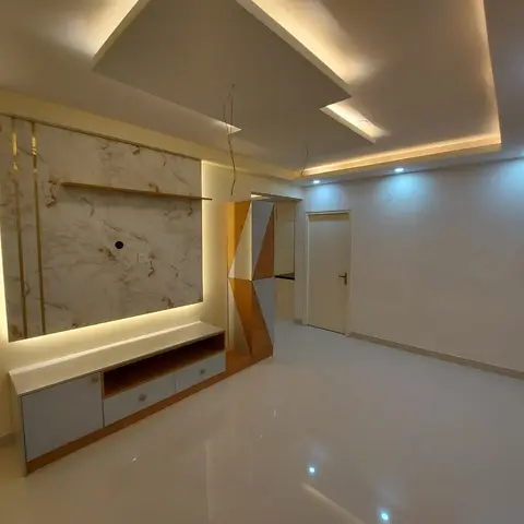 Empty living room with a backlit marble-effect TV feature wall trimmed in brass, a faceted geometric decorative pillar, and a stepped cove-lit false ceiling.