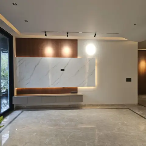 Empty living room with a backlit marble TV feature wall flanked by wood veneer panels, a floating console unit, and a glossy marble floor with a border inlay.
