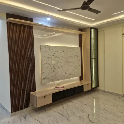 Empty living room with a backlit marble-look panel floating on the TV wall between dark fluted wood pillars and a green backlit glass strip