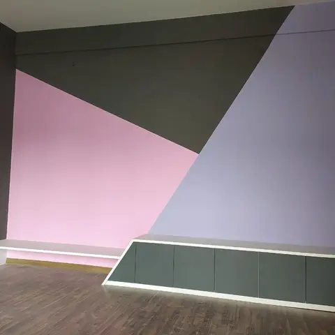 Empty living room with a bold pink, purple and charcoal triangular color-block feature wall above a long low grey and white console.