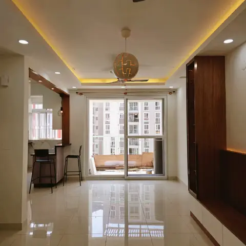 Empty living room with a cove-lit ceiling in warm yellow LED lighting, a spherical cutout pendant light, a sliding glass balcony door