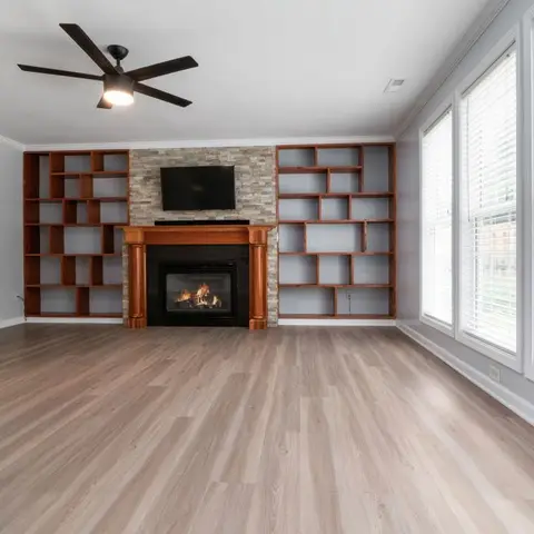 Empty living room with a stone-clad fireplace flanked by asymmetric wood bookshelves and a wall of windows with blinds