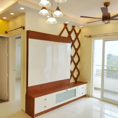 Empty living room with a teak-framed white TV back panel flanked by a diamond-lattice wooden fretwork strip, a white two-drawer console below
