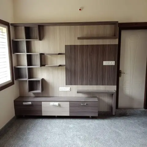 Empty living room with an asymmetric dark-wood cubby shelf and TV panel wall, a stepped cove ceiling, and speckled grey terrazzo flooring.