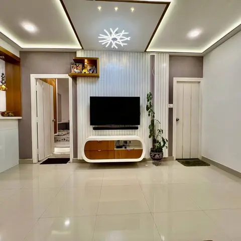 Empty living room with an oval floating TV console beneath a fluted white panel wall, a cove-lit ceiling with a sunburst pendant light