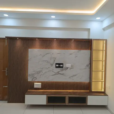 Empty living room with an unoccupied TV bracket on a white veined slab set into a wall of walnut fluted panelling, a brown marble ledge running over it