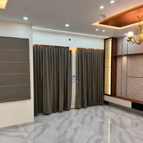 Empty living room with floor-to-ceiling brown curtains, a marble-clad TV feature wall with a lit glass display niche, and a small crystal chandelier