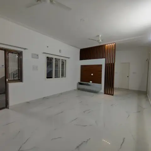 Empty living room with white marble flooring, a wood-slat partition screen beside a wood-panelled TV wall, and a grilled window