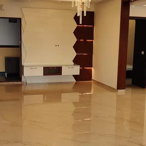Empty new-build Indian living room with a cove-lit stepped false ceiling, crystal drop chandelier, and a dark wood chevron-panelled TV feature wall