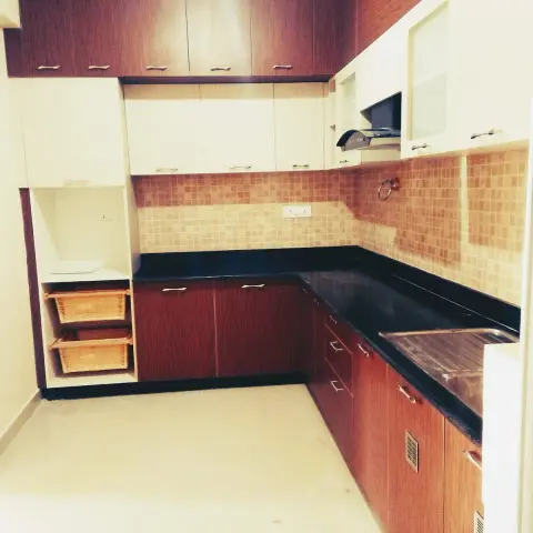 Empty older L-shaped kitchen in rosewood laminate paired with cream shutters, black granite counter with cut drainboard grooves beside the sink