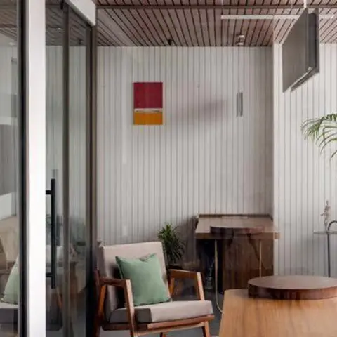 Enclosed balcony sit-out with a wood-slat ceiling, a mid-century armchair with a green cushion, and a framed abstract print on the slat wall