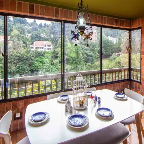Enclosed brick sunroom dining nook with a white table set with blue-patterned plates and a decorative birdcage, overlooking green hillside views