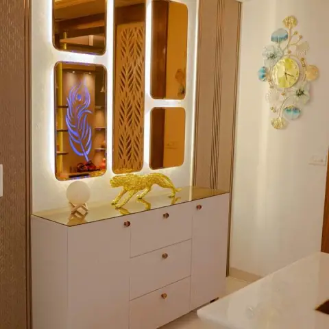 Entrance console vignette with a backlit asymmetric mirror-and-jaali panel cluster, a white console cabinet with brass hardware, and a gold leopard figurine.