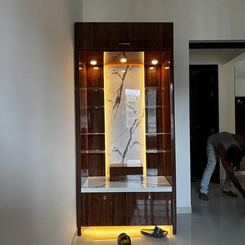 Entrance display unit in high-gloss walnut veneer with glass shelves and a backlit book-matched marble niche, slippers left at its base.