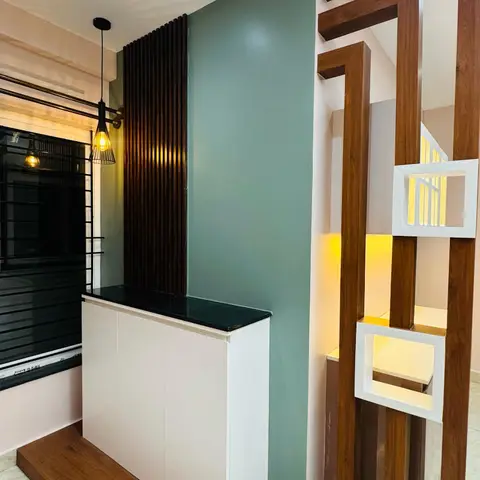 Entrance foyer console cabinet with a black stone top on a wood platform, beside a sage-green accent wall and a decorative wood-slat partition with lit