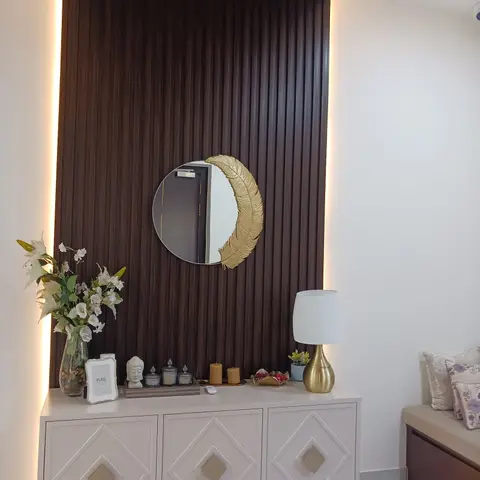 Entrance foyer console styled with a round gold-feather mirror against a fluted dark-wood panel wall lit by cove lighting