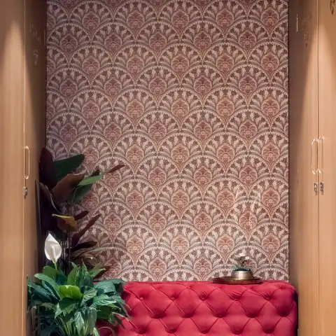 Entrance foyer nook with a burgundy damask wallpaper wall, a red tufted velvet bench, and potted plants, framed by open wardrobe doors on either side.