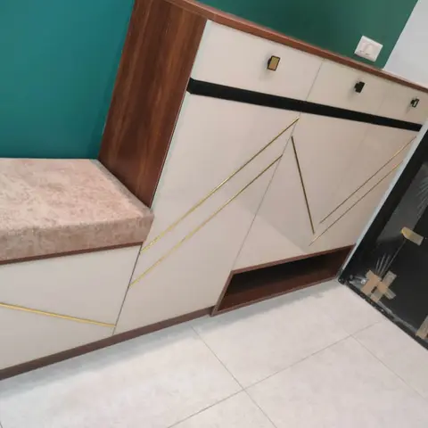 Entrance foyer shoe cabinet with a cushioned bench seat, gold geometric inlay on cream gloss shutters, and a teal accent wall beside the main door.