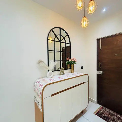 Entrance foyer with a cluster of three gold cage pendant lights above an arched black-framed mirror and a curved white shoe cabinet styled with pampas grass