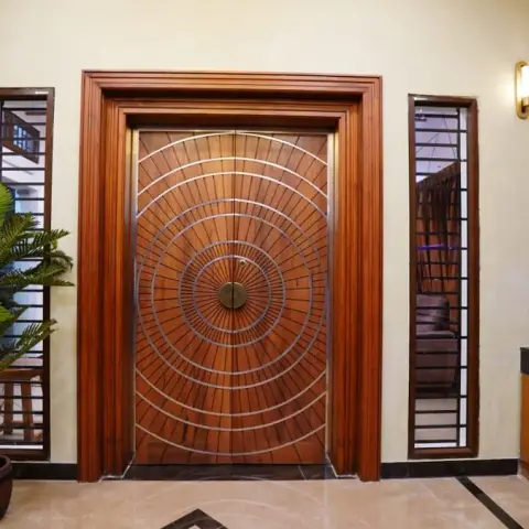 Entrance foyer with a concentric circular-groove solid wood main door with metal inlay banding, flanked by wall sconces and a floor medallion inlay
