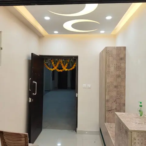 Entrance foyer with a crescent-moon cutout cove-lit false ceiling, a dark wood-finish main door dressed with a marigold toran