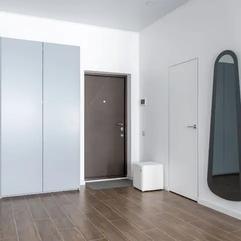 Entrance foyer with a curved pale blue-grey storage cabinet, a dark wood-effect main door, and a large teardrop-shaped wall mirror.