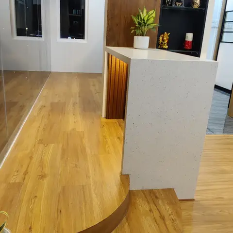 Entrance foyer with a curved wood platform step, a white quartz-clad column, and a backlit black display niche holding pooja idols and a plant.
