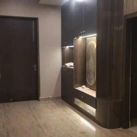 Entrance foyer with a dark wood-veneer shoe and wardrobe unit featuring a backlit oval mirror niche, beside the main door and a fluted panel wall.