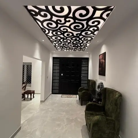 Entrance foyer with a dramatic black CNC-cut backlit false ceiling, a black slatted main door and a pair of dark green velvet wingback chairs.