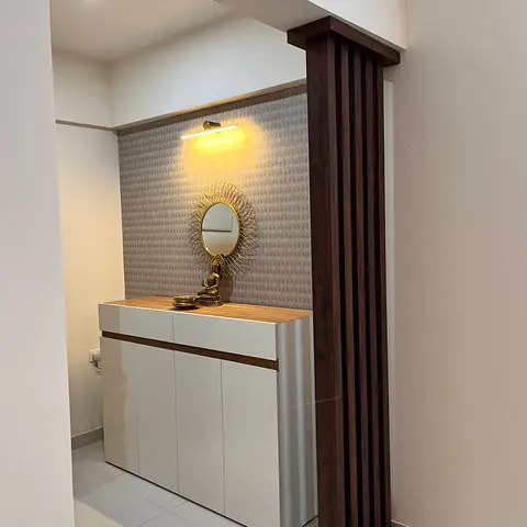 Entrance foyer with a fluted dark-wood partition column beside a glossy white shoe cabinet topped with a sunburst mirror and brass Buddha statue against