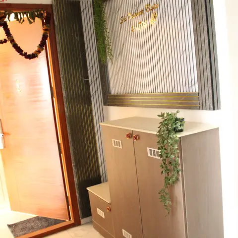 Entrance foyer with a fluted stone-and-brass-inlay name-plate wall above a wood-tone shoe cabinet trailed by a potted vine.