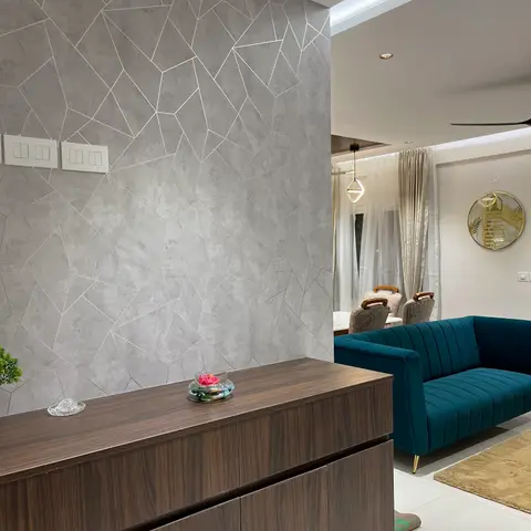 Entrance foyer with a fractured-pattern grey textured feature wall behind a dark wood console table, opening into a living room with a teal channel-tufted sofa.