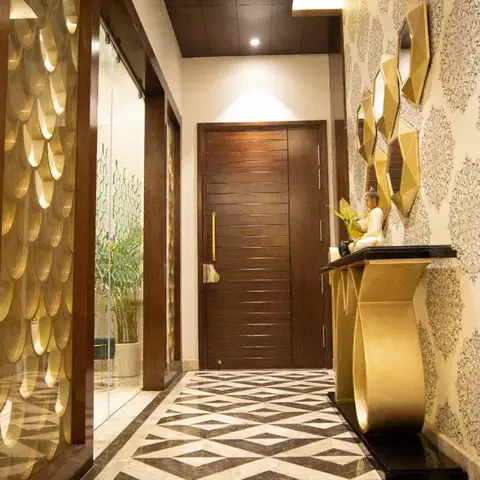 Entrance foyer with a gold scalloped jaali wall screen, geometric marble floor inlay, and a gold console table beneath a cluster of angular mirrors.