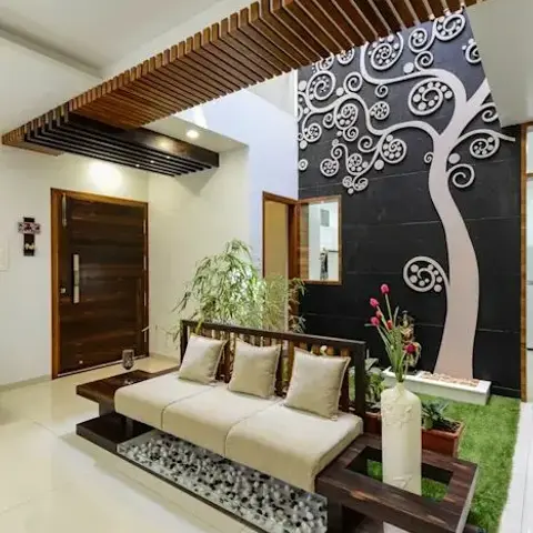 Entrance foyer with a low teak platform daybed over a pebble-filled recess, facing a double-height black stone wall carrying a white swirl-tree motif